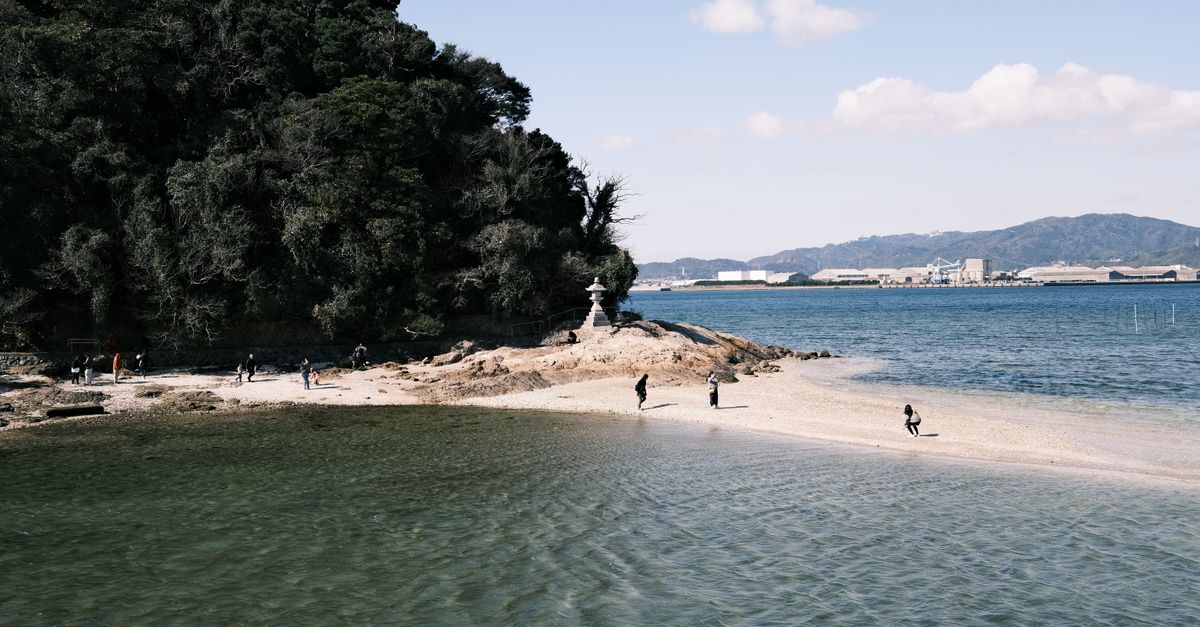 Explore the tranquil seaside view of Gamagōri, Aichi, Japan with distant cityscapes and sandy islands.